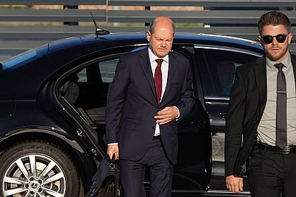 Bundeskanzler Olaf Scholz (l, SPD) kommt zum Start einer zweitägigen Reise auf dem militärischen Teil des Flughafens Berlin Brandenburg BER an und steigt aus einer Limousine.